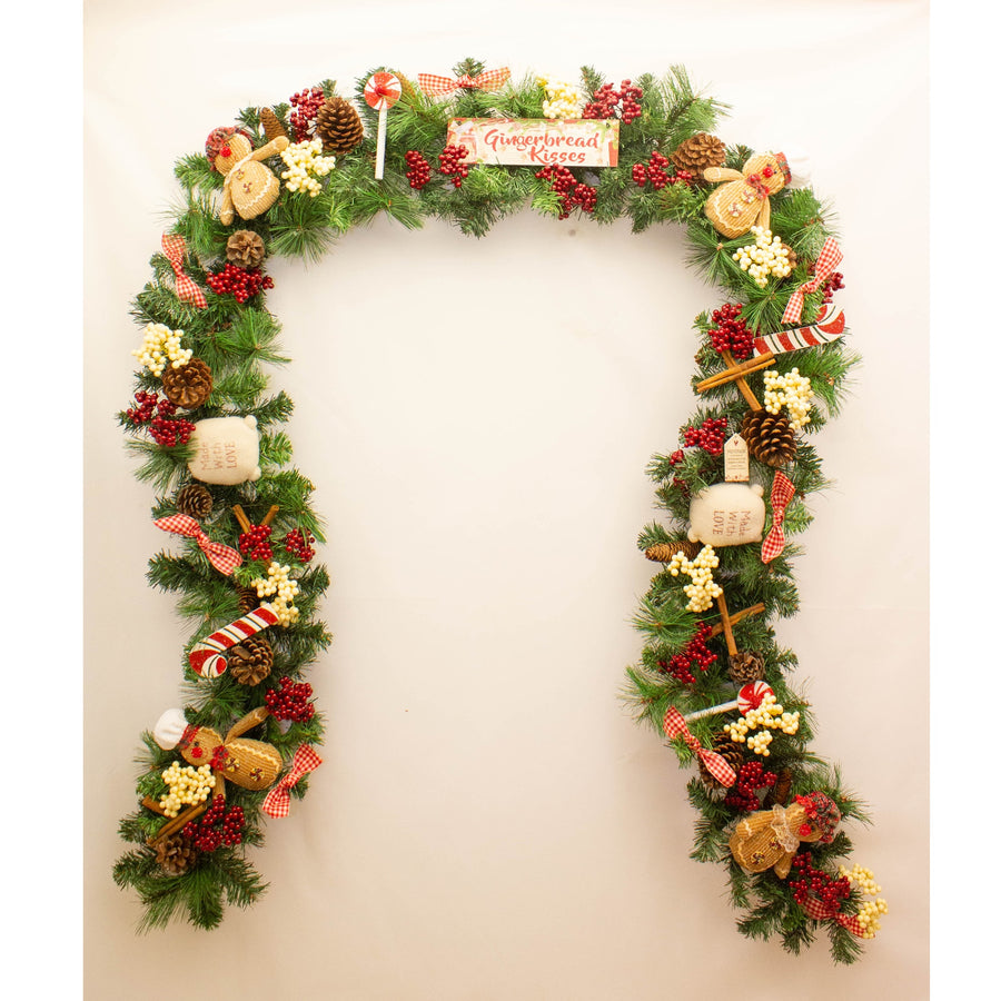 A decorative gingerbread-themed garland featuring Christmas ornaments, pine branches, and festive accents.