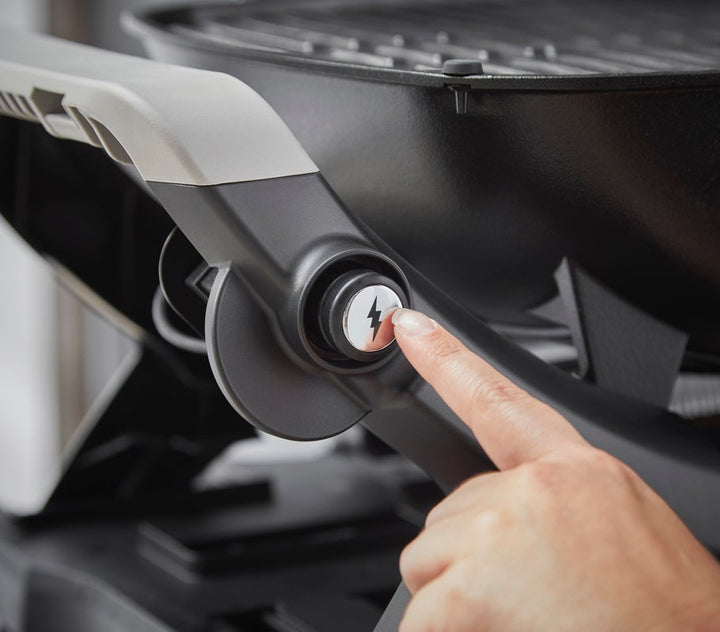 A hand pushing  a Weber Q1200N barbecue ignition button