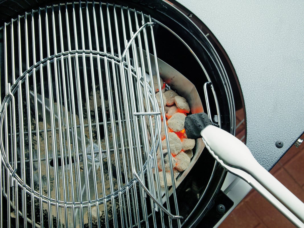 a tongs putting a coal into a Weber charcoal BBQ