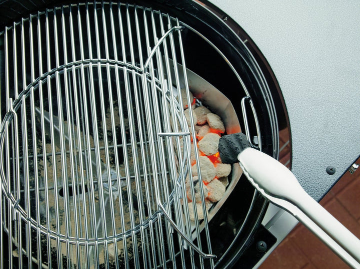 a tongs putting a coal into a Weber charcoal BBQ