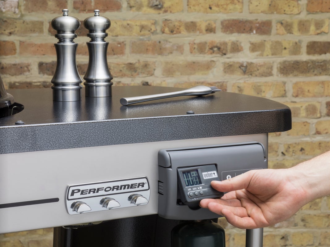 a hand pulling out a Weber Performer Deluxe timer