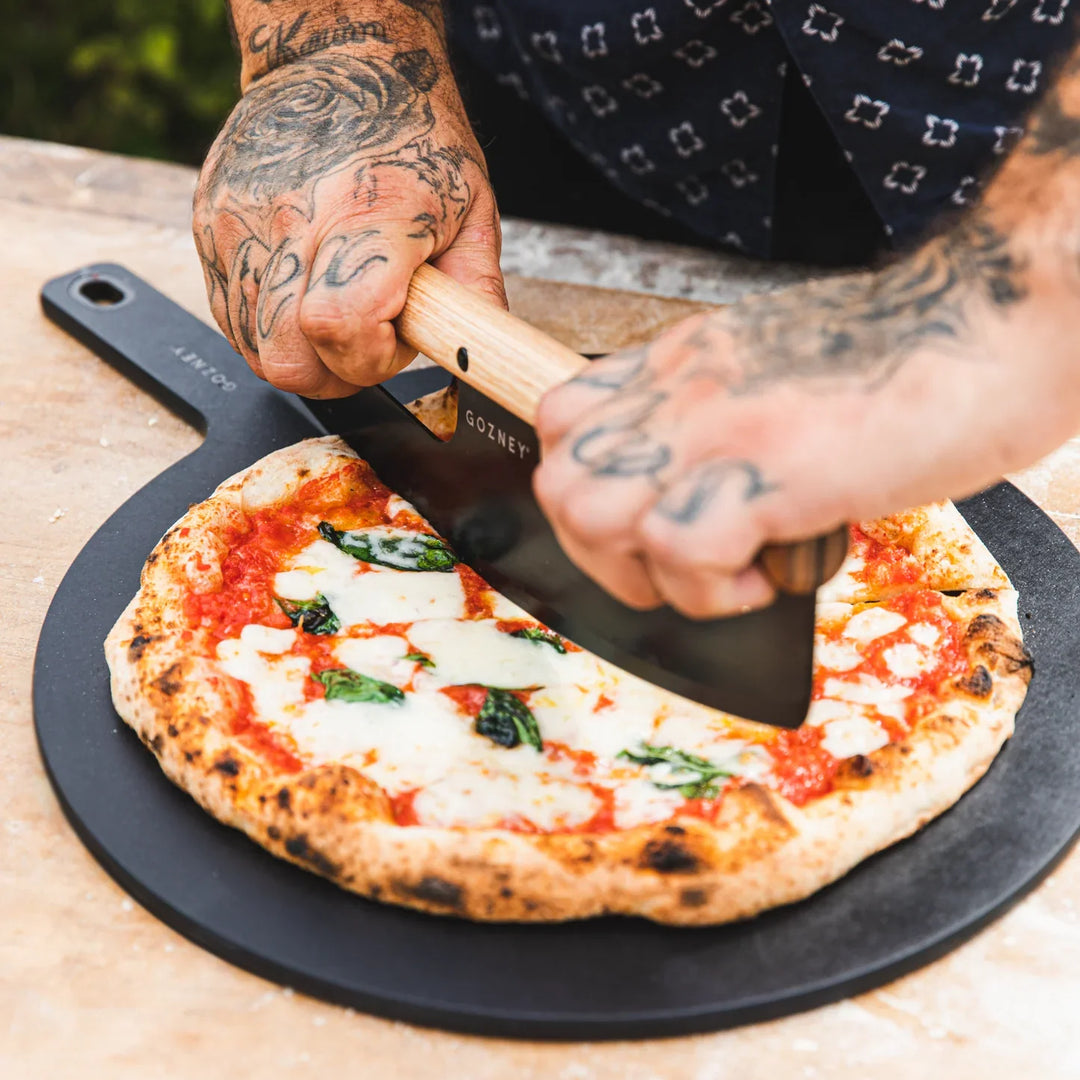 A Person cutting a pizza with a Gozney pizza cutter accessory