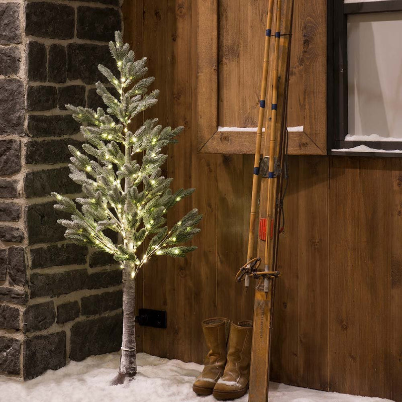 Decorative Christmas tree with lights next to a wooden wall with skis and boots.