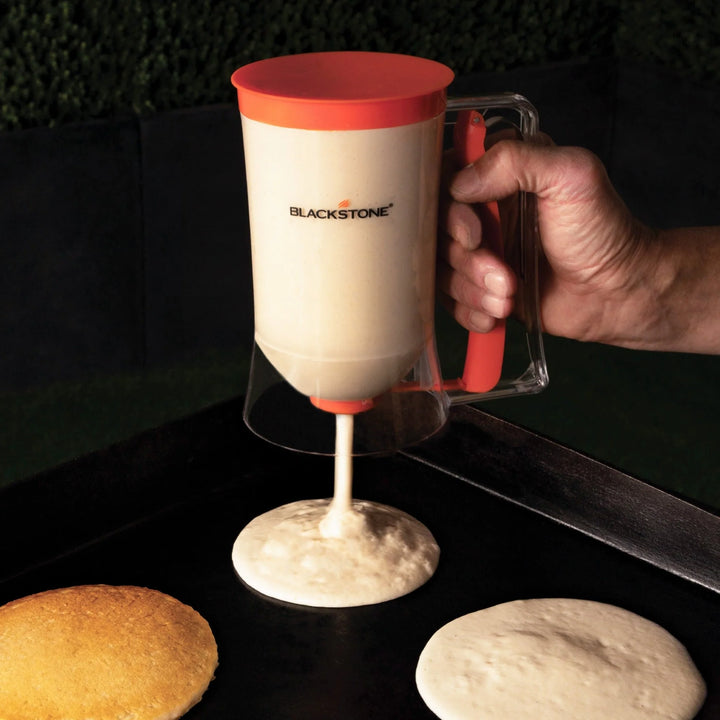 Person using a Blackstone breakfast batter maker to cook pizza dough on a black surface.