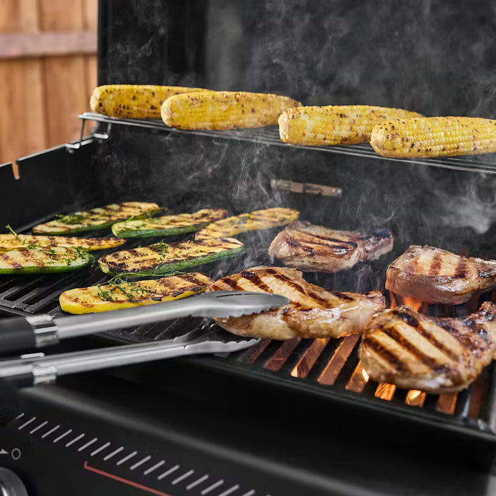 Grilling vegetables and meats on a Weber gas barbecue with tongs.