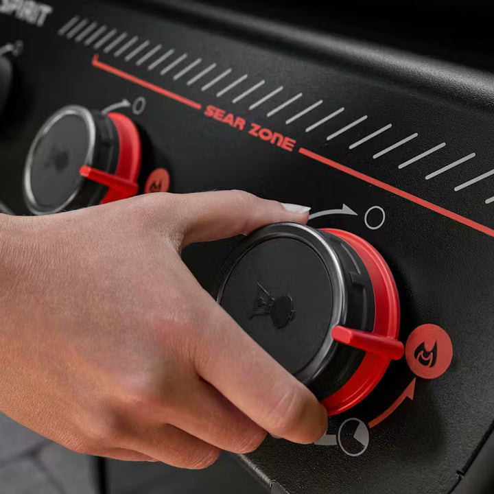 Hand adjusting Weber gas controller on a black and red control panel with 'Weber Sear Zone' branding.
