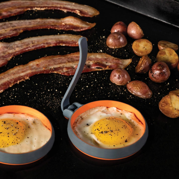 Eggs in Blackstone nest cookers with bacon and potatoes on a grill