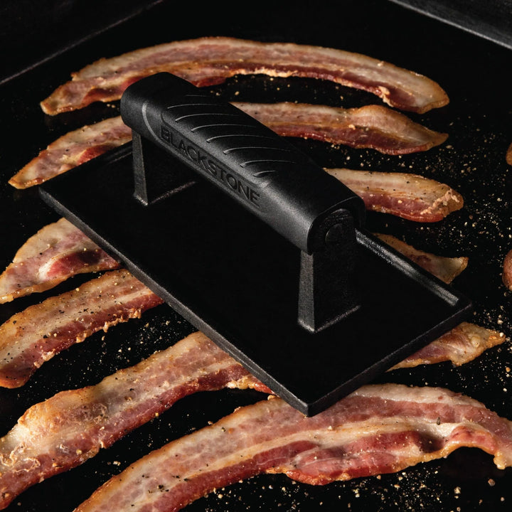Blackstone bacon press on a grill with bacon slices