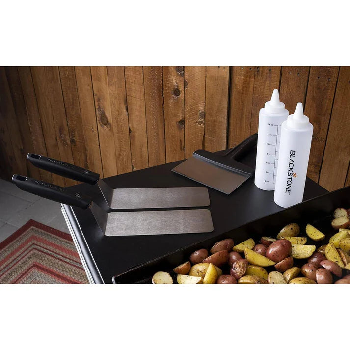 Blackstone Grill with cooking utensils and potatoes against a wooden background