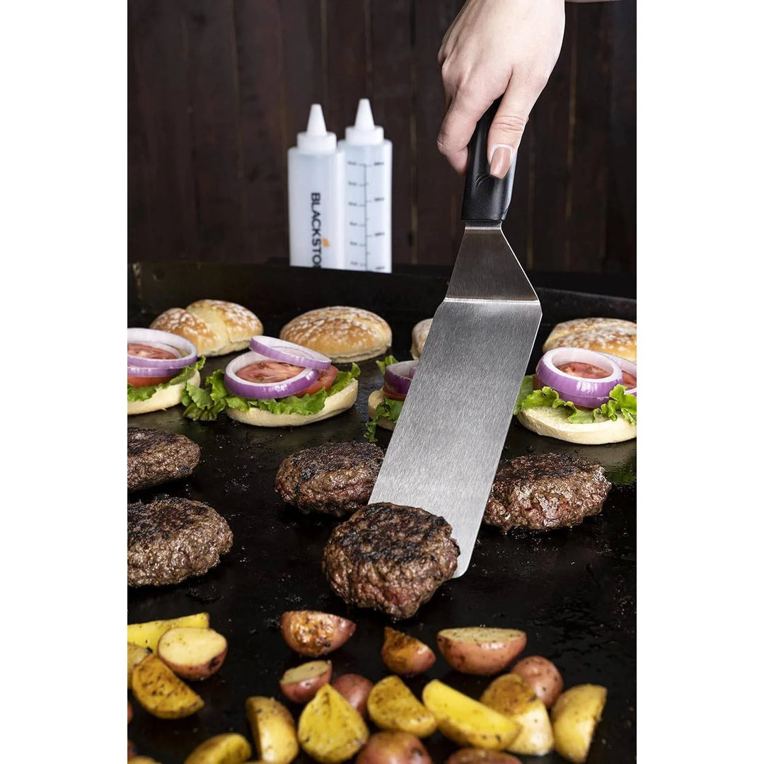 Person grilling burgers and potatoes with a Blackstone spatula, Blackstone logo visible.