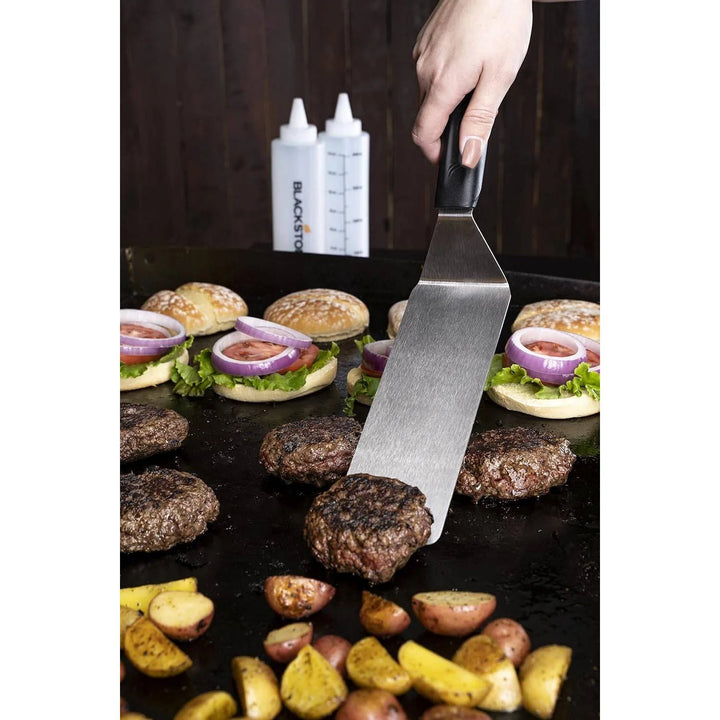 Person grilling burgers and potatoes with a Blackstone spatula, Blackstone logo visible.