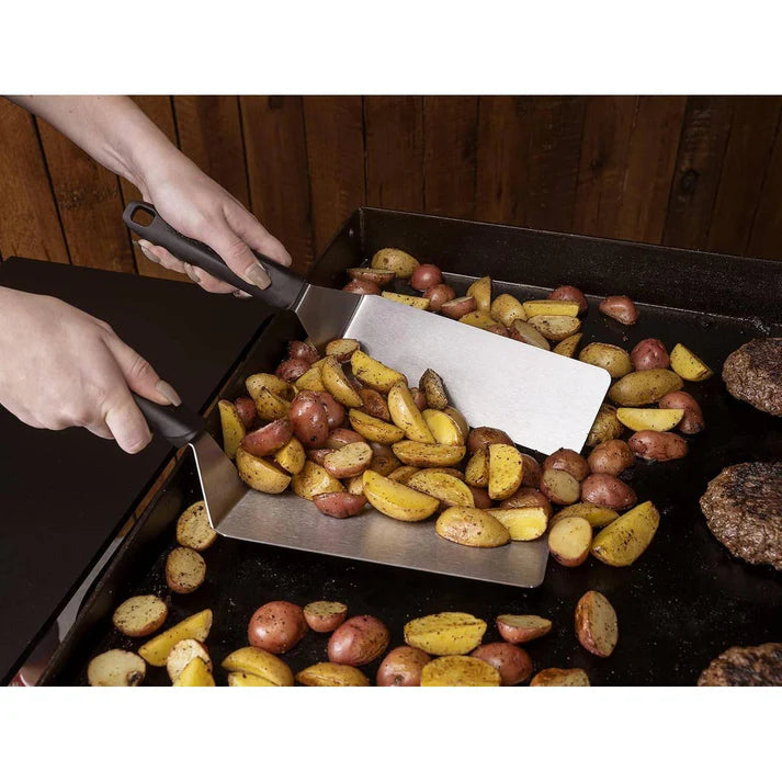 Person using Blackstone tongs to handle roasted potatoes on a baking sheet with a wooden background