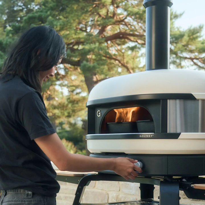 Person using a Gozney Dome Gen 2 pizza oven outdoors in Ireland with trees in the background