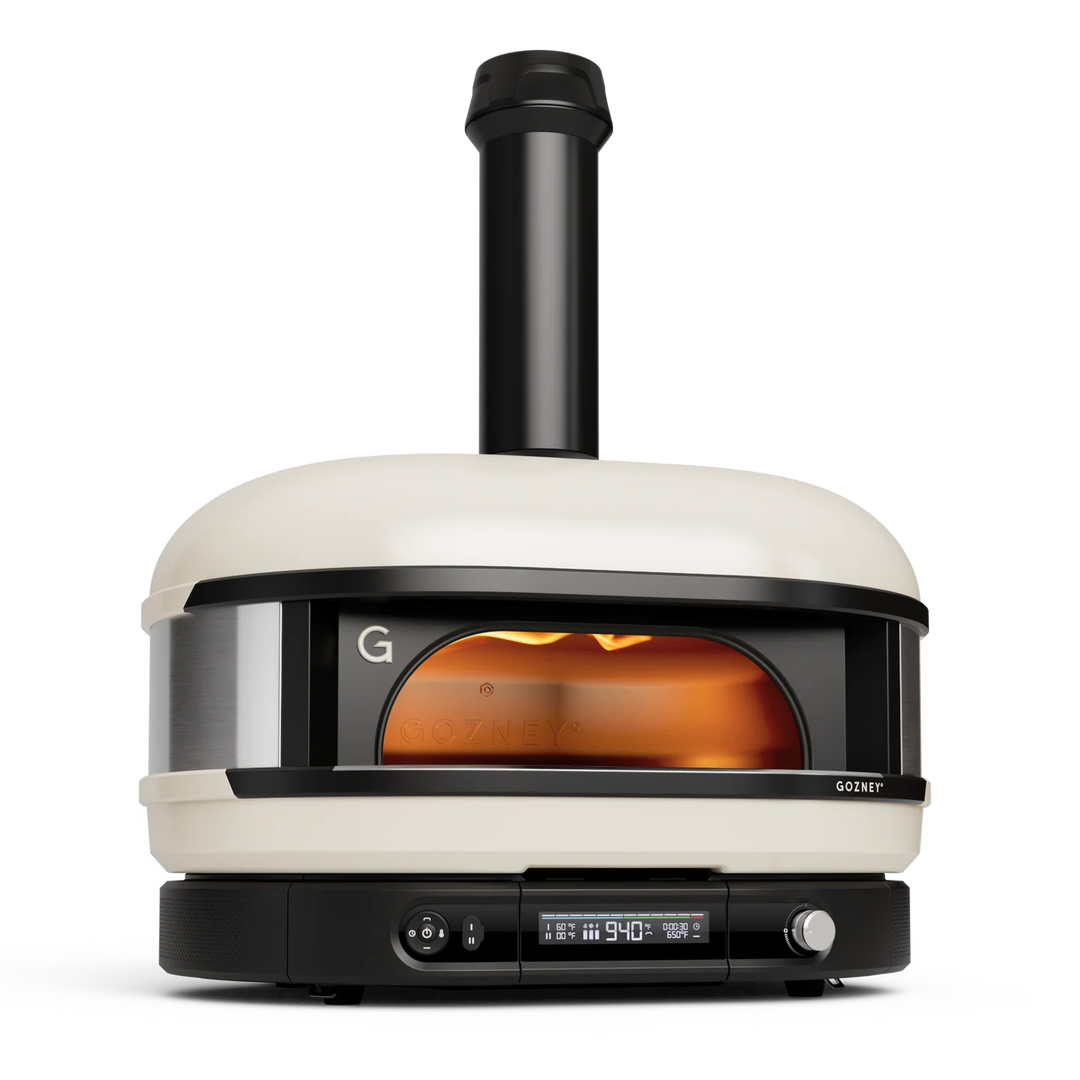 A Gozney pizza oven with a cream-colored body, black accents, and a visible flame inside, shown on a clean white background.
