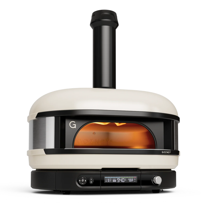 A Gozney pizza oven with a cream-colored body, black accents, and a visible flame inside, shown on a clean white background.