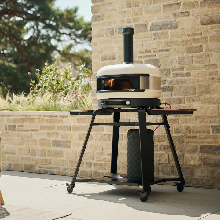 Gozney Dome pizza oven on a stand against a brick wall.