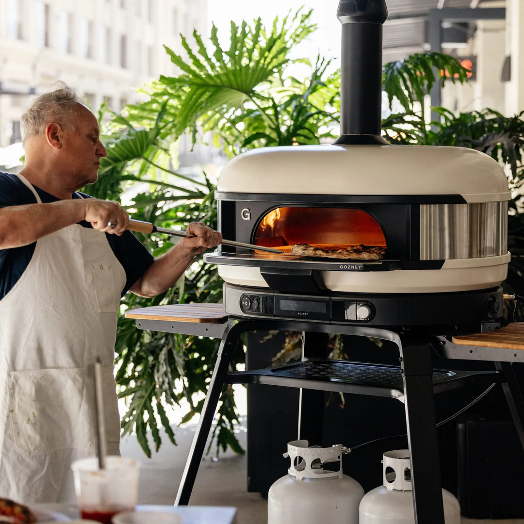 Person using a Gozney Dome XL pizza oven outdoors with plants in the background