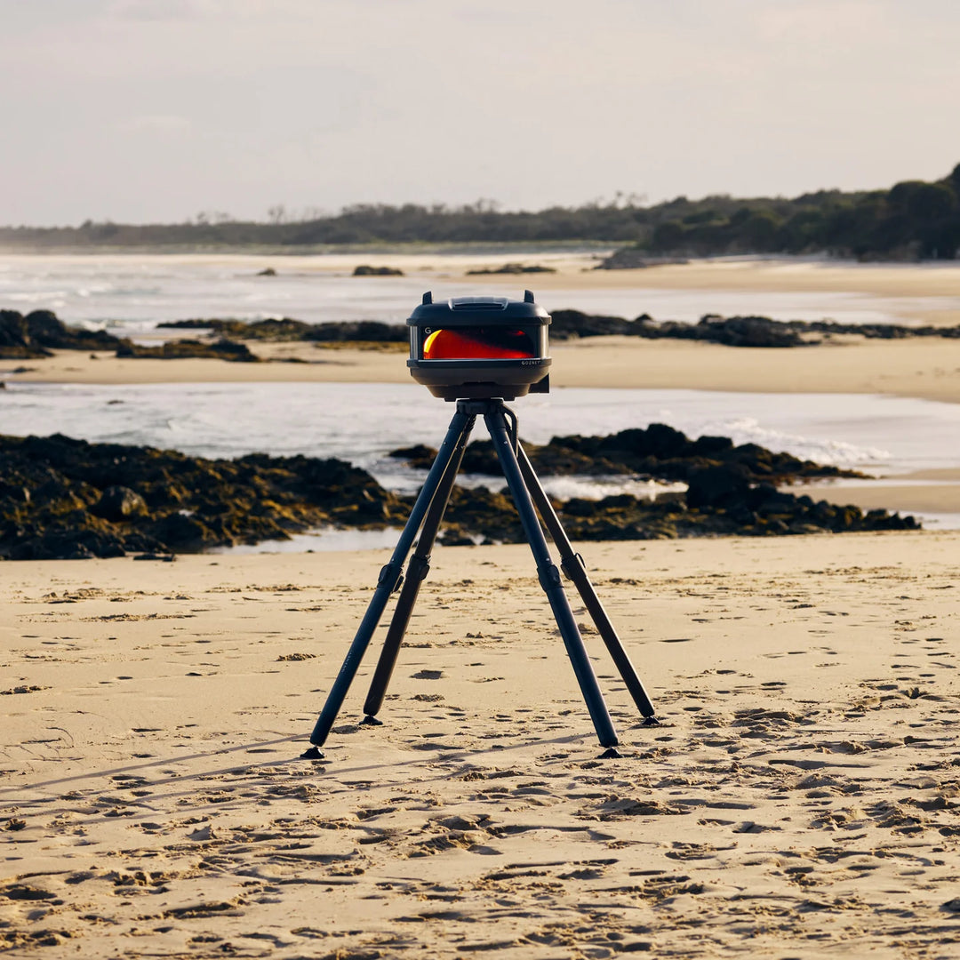Gozney pizza oven on a tripod at the beach in Ireland with ocean and rocks in the background