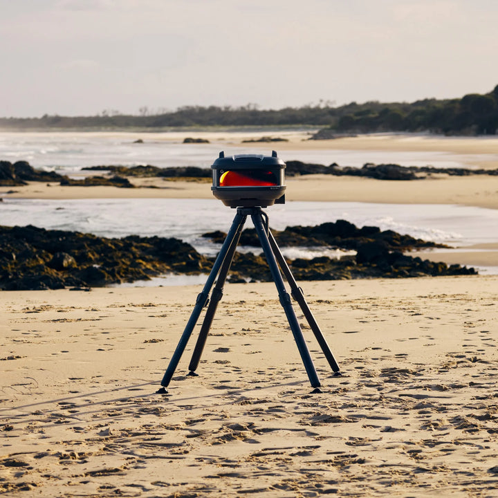 Gozney pizza oven on a tripod at the beach in Ireland with ocean and rocks in the background