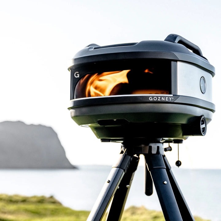 Gozney thread pizza oven on a tripod with flames inside, set against a natural irish landscape.