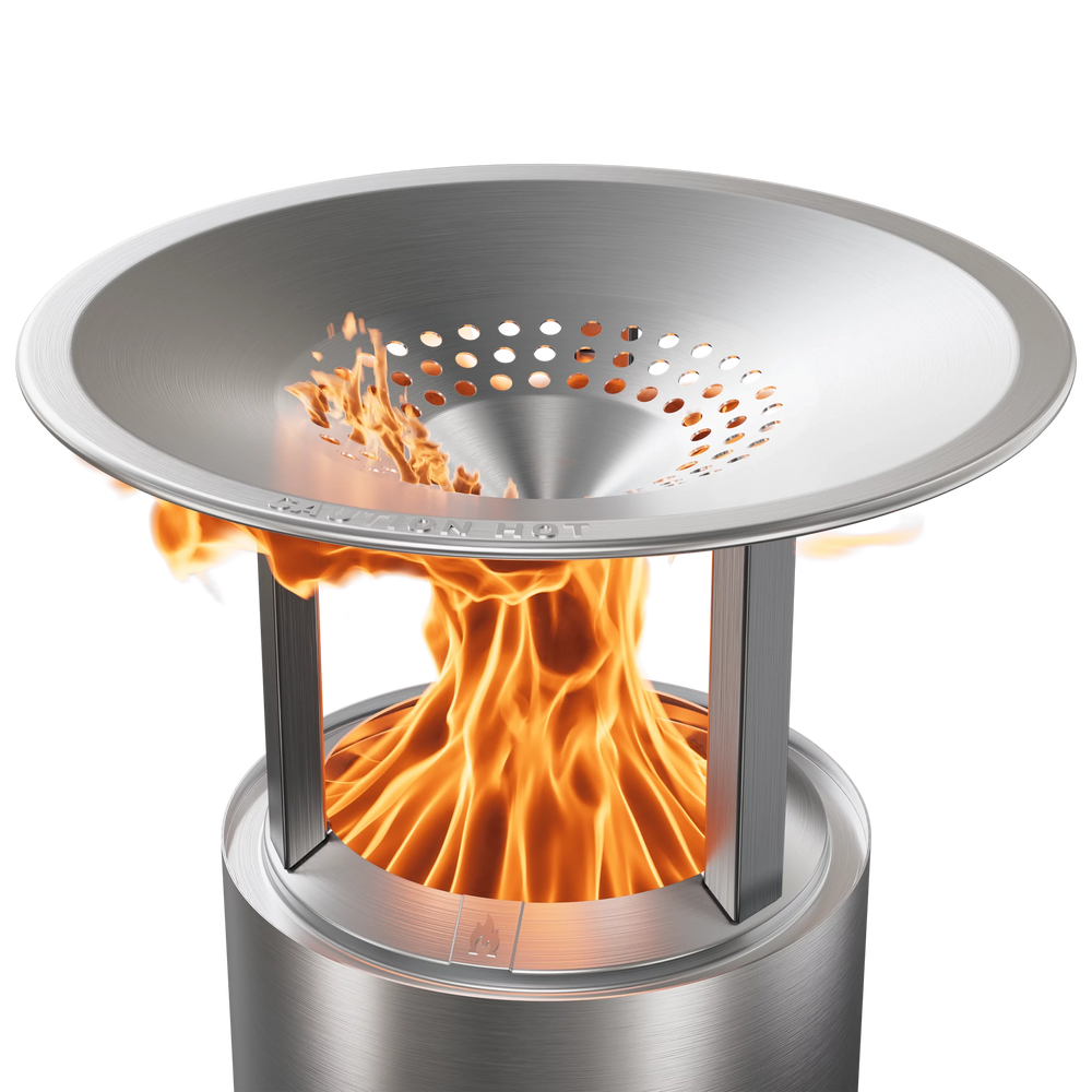 A silver stainless steel heat deflector for a fire pit with visible flames coming out from the top, indicating heat distribution.