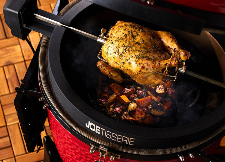Whole chicken roasting on the Kamado Joe Joetisserie with a pan of vegetables below catching the drippings