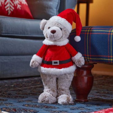 Plush Christmas teddy bear in a Santa outfit on a carpeted floor with a blurred background